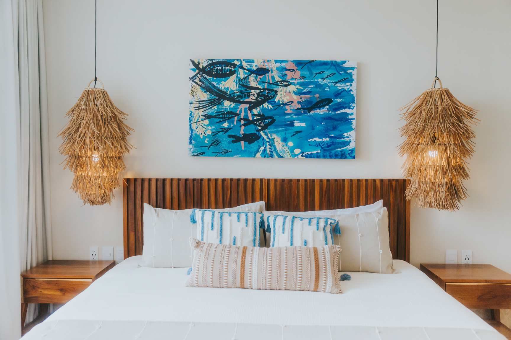 Bedroom with slatted wood headboard, ocean artwork and palm pendant lights