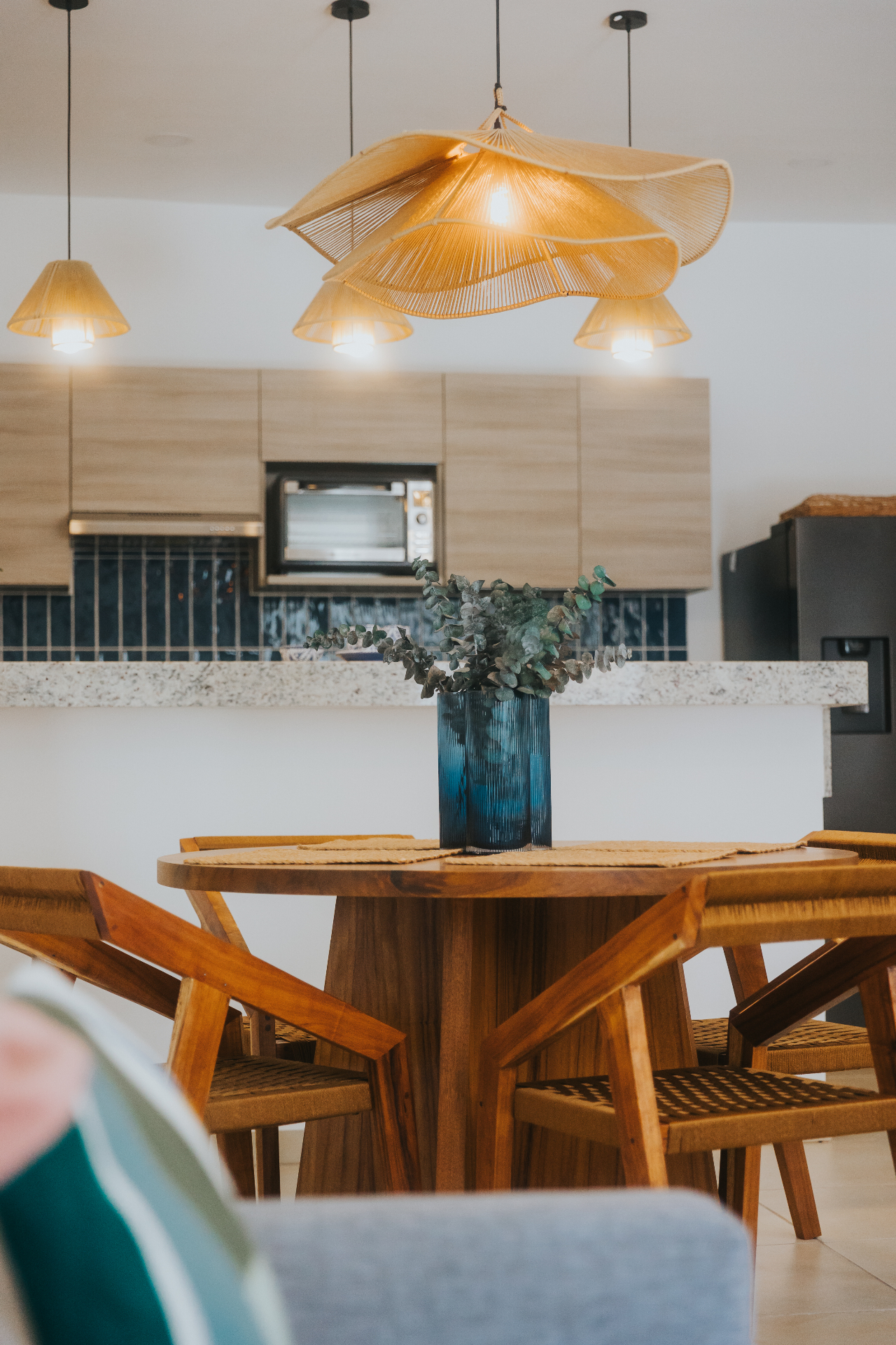 Sculptural rattan pendant above a tzalam dining table with woven chairs and eucalyptus