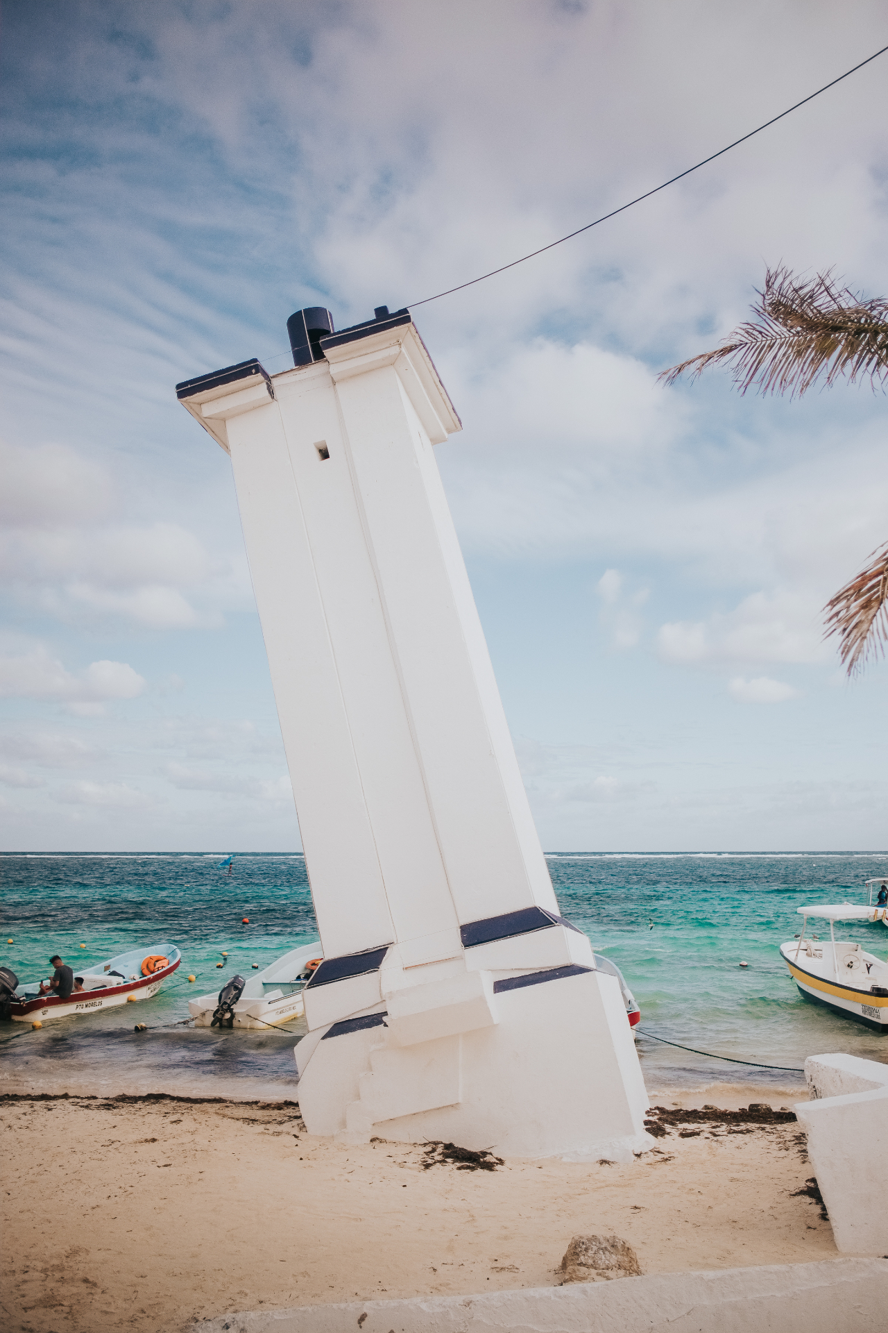 The iconic leaning lighthouse of Puerto Morelos with turquoise Caribbean water and fishing boats